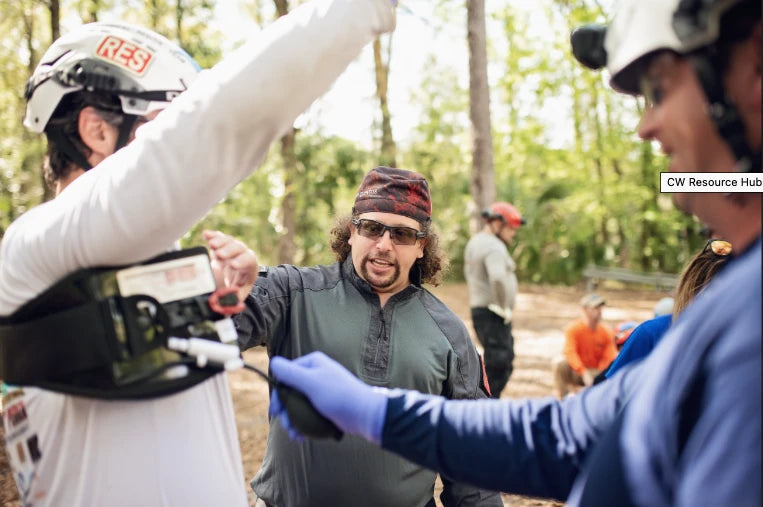 Compression Works AAJT-S-001 abdominal tourniquet being positioned by an instructor on a volunteer during an outdoor wooded rescue training scenario