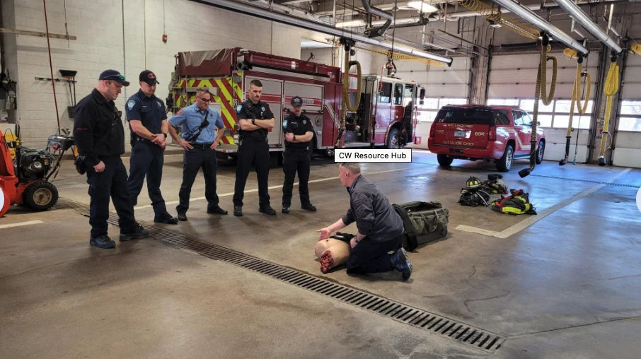 Compression Works AAJT-S-001 application demonstration on a training mannequin by an instructor with firefighters observing inside the fire station.