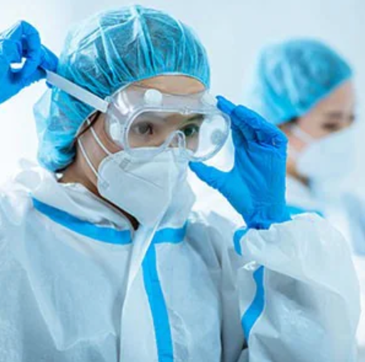 woman wearing eye protection, hair bonnet, and isolation gown.